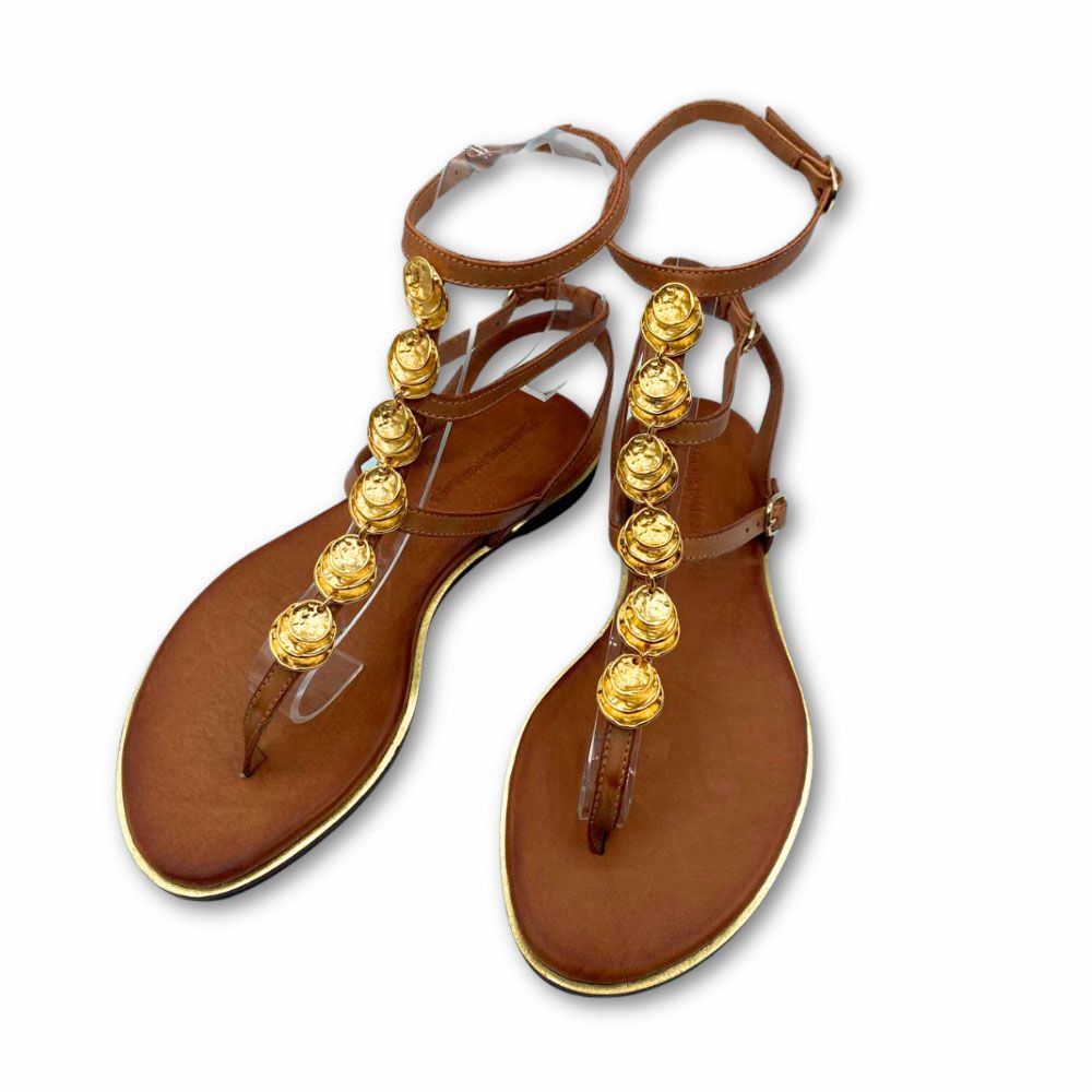 Sandalias griegas de piel color cuero, con chapas doradas en tira central. Cierre con hebillas. Suela plana y tacón bajo de Exé.