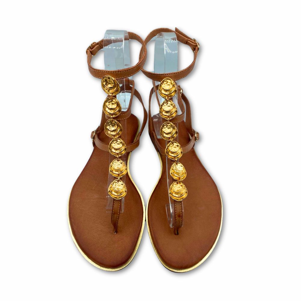 Sandalias griegas de piel color cuero, con chapas doradas en tira central. Cierre con hebillas. Suela plana y tacón bajo de Exé.