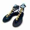 Sandalias griegas de piel color negro, con chapas doradas en tira central. Cierre con hebillas. Suela plana y tacón bajo de Exé.